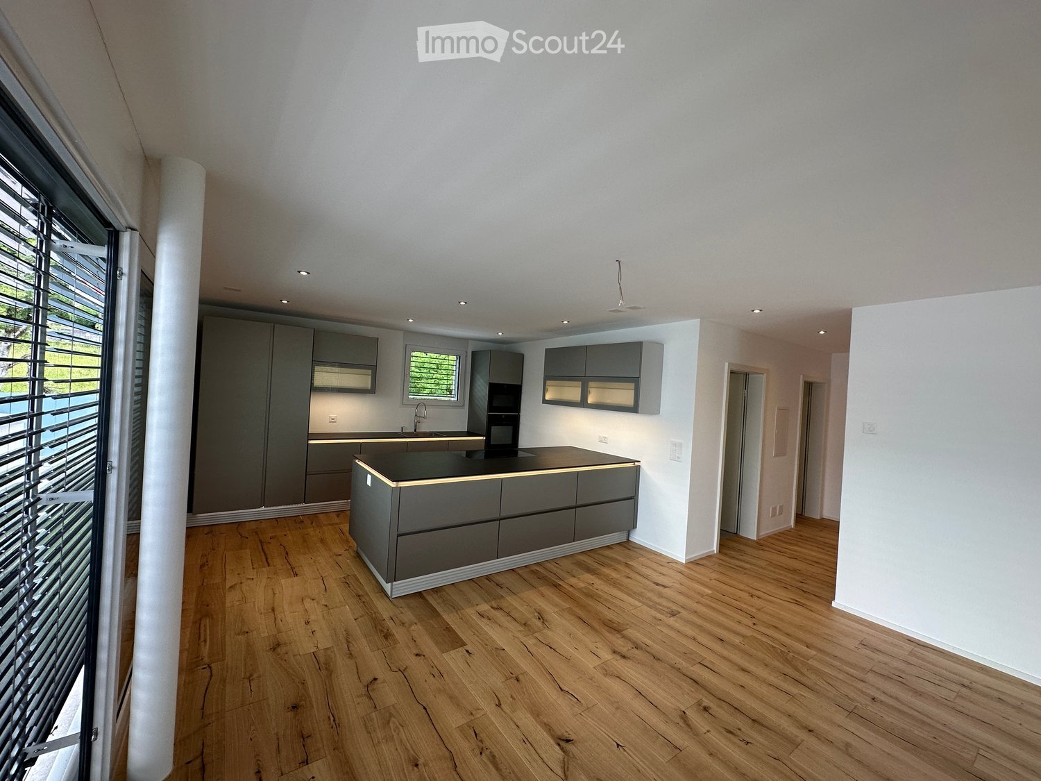 Modern kitchen with central island, gray cabinets, white walls, wooden floor, bright lighting