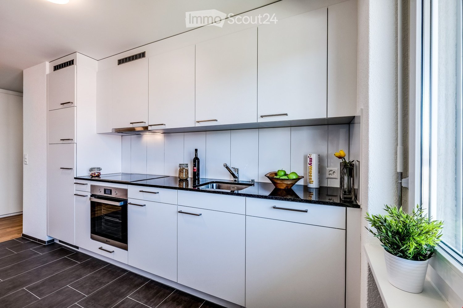 modern white kitchen, white cupboards, wooden floor, granite kitchen table, black countertops, stainless steel sink, faucet, white refrigerator, oven, dishwasher, and washing machine