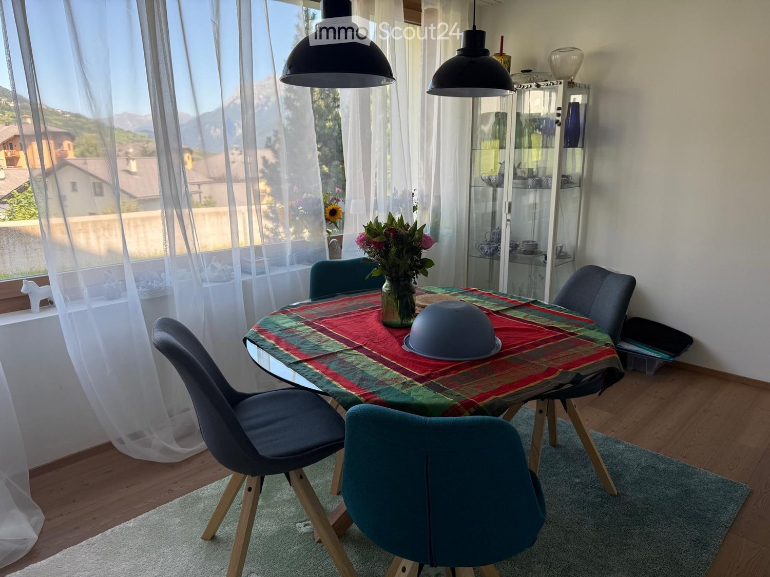 dining table with chairs, round glass table, flower vase, wooden floor, table runner, decorative bowl, view of mountains through large windows