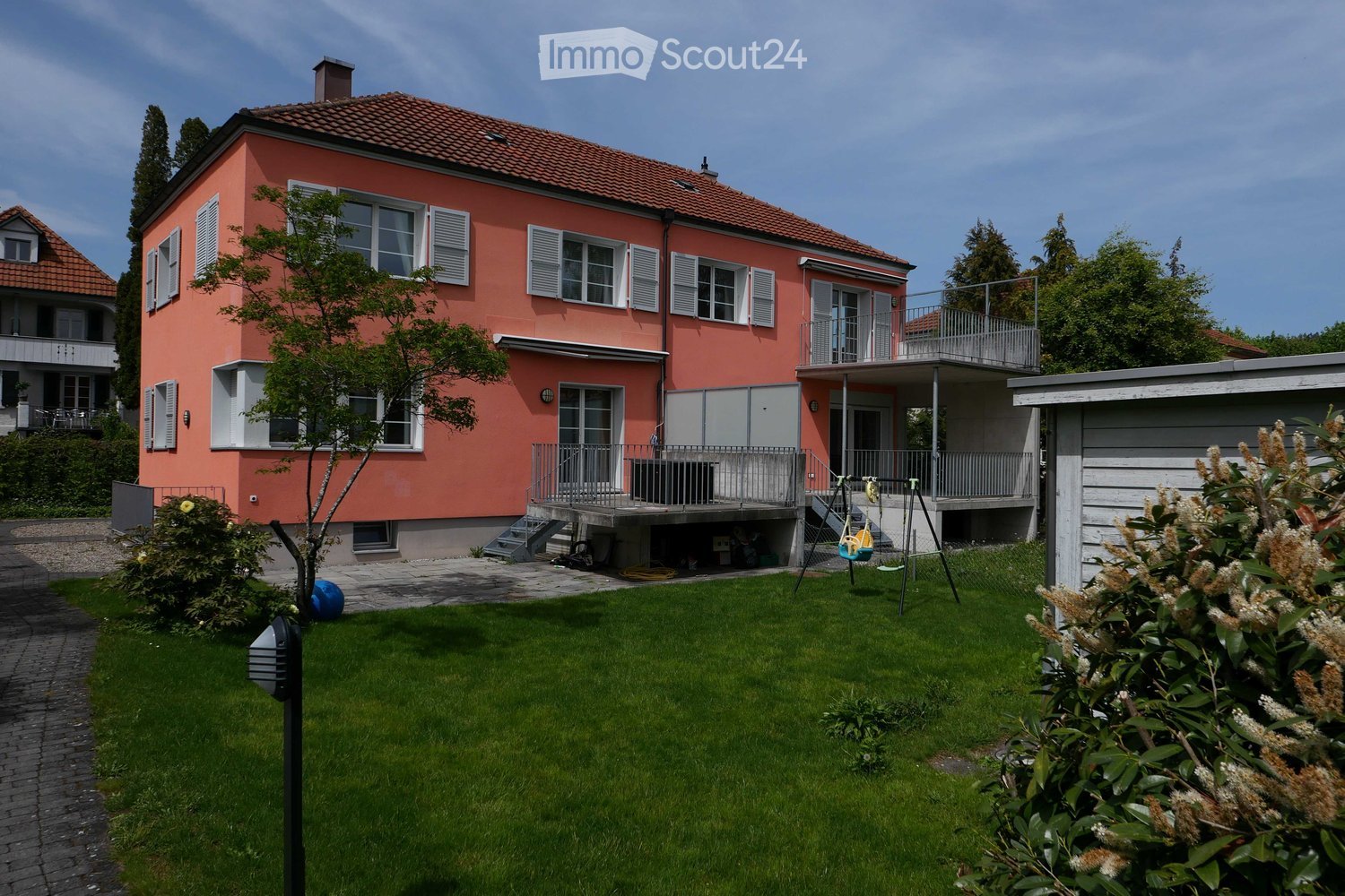 2-story house, terracotta exterior, multiple balconies, yard with grass and plants, wooden storage shed, brick driveway