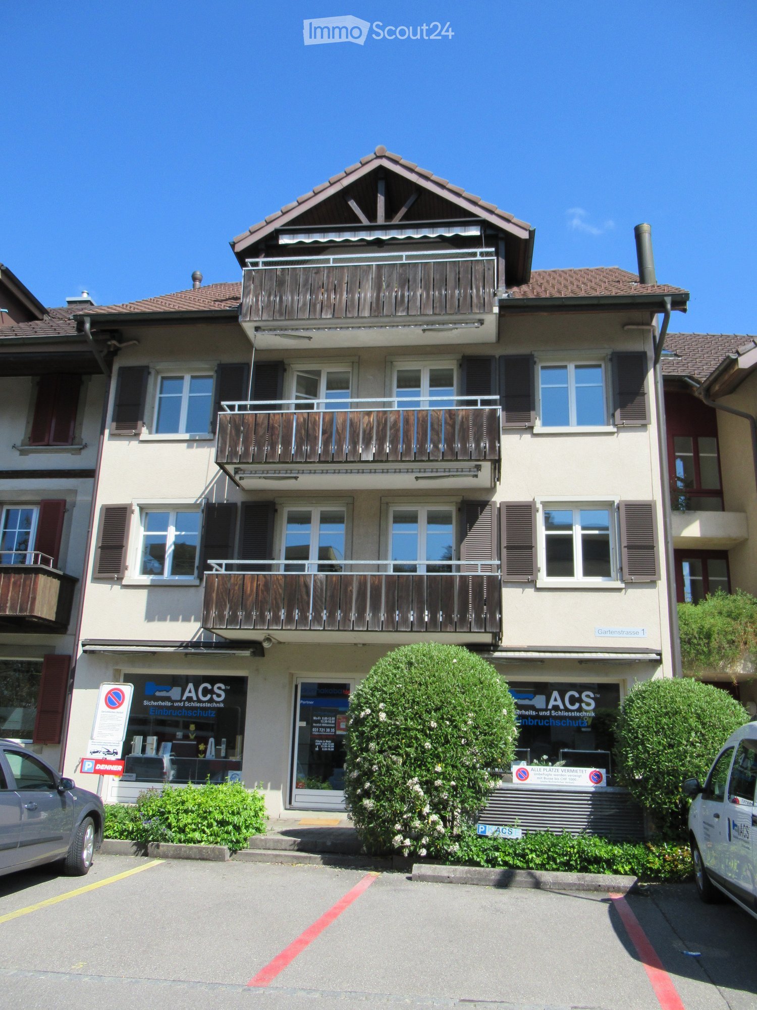 3 story building, balconies on 2nd and 3rd floors, large front yard with plants, parking lot in front