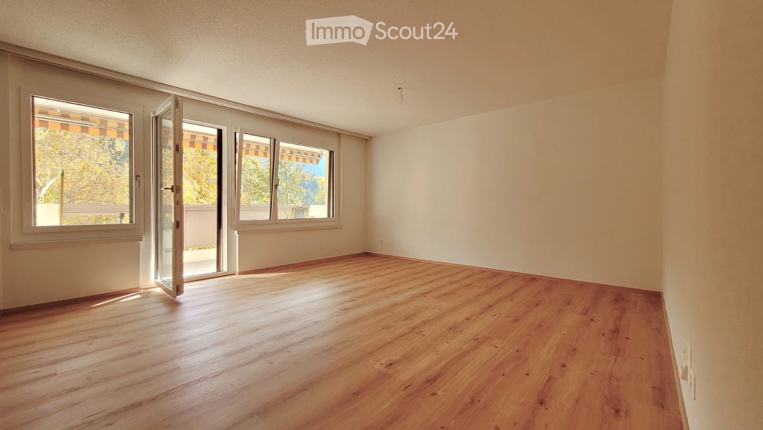 large room, wooden floor, open door to balcony, large windows