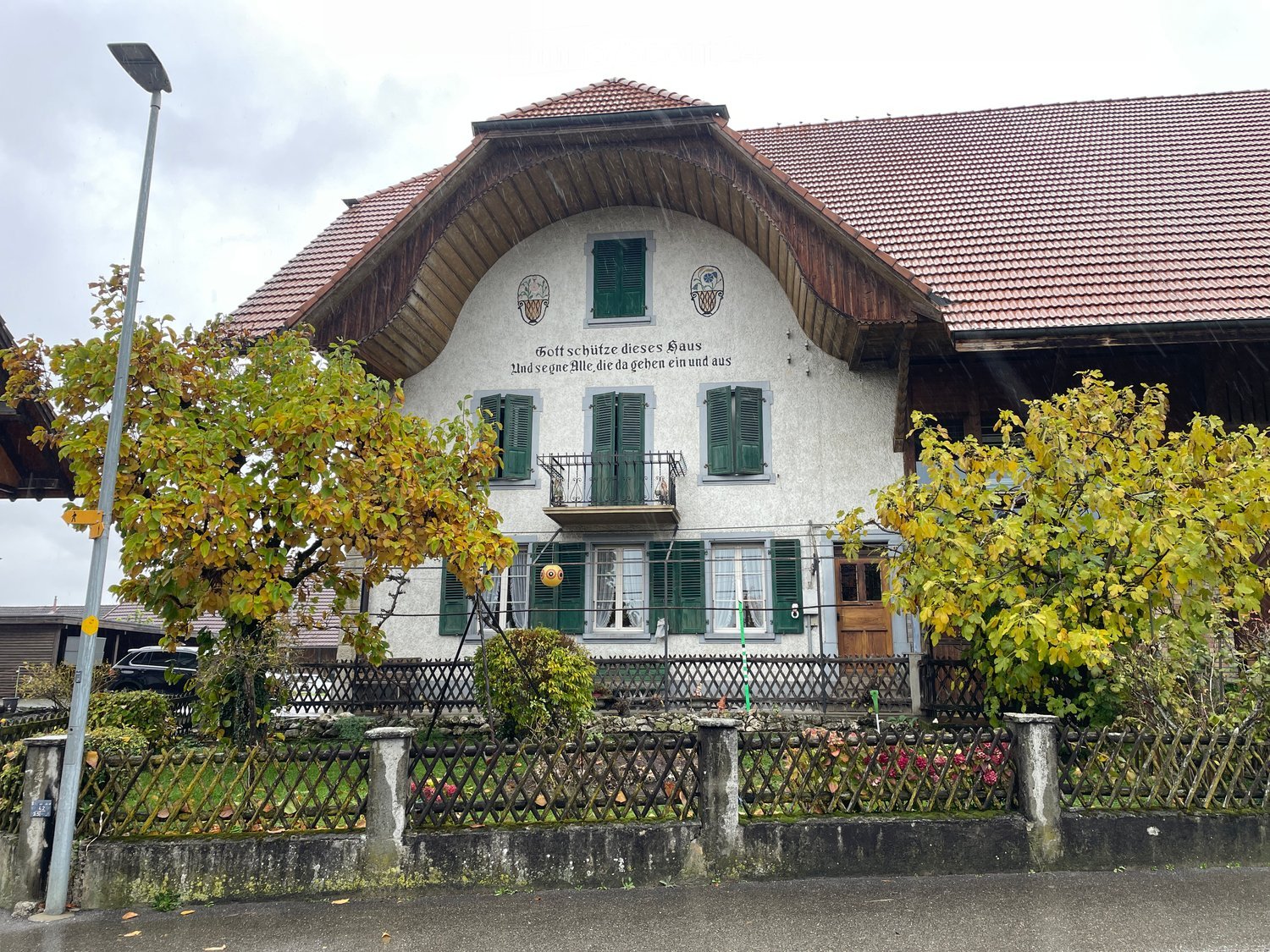 Traditional architectural design, red roof, green shutters, balcony, multiple windows, fence in front of the house