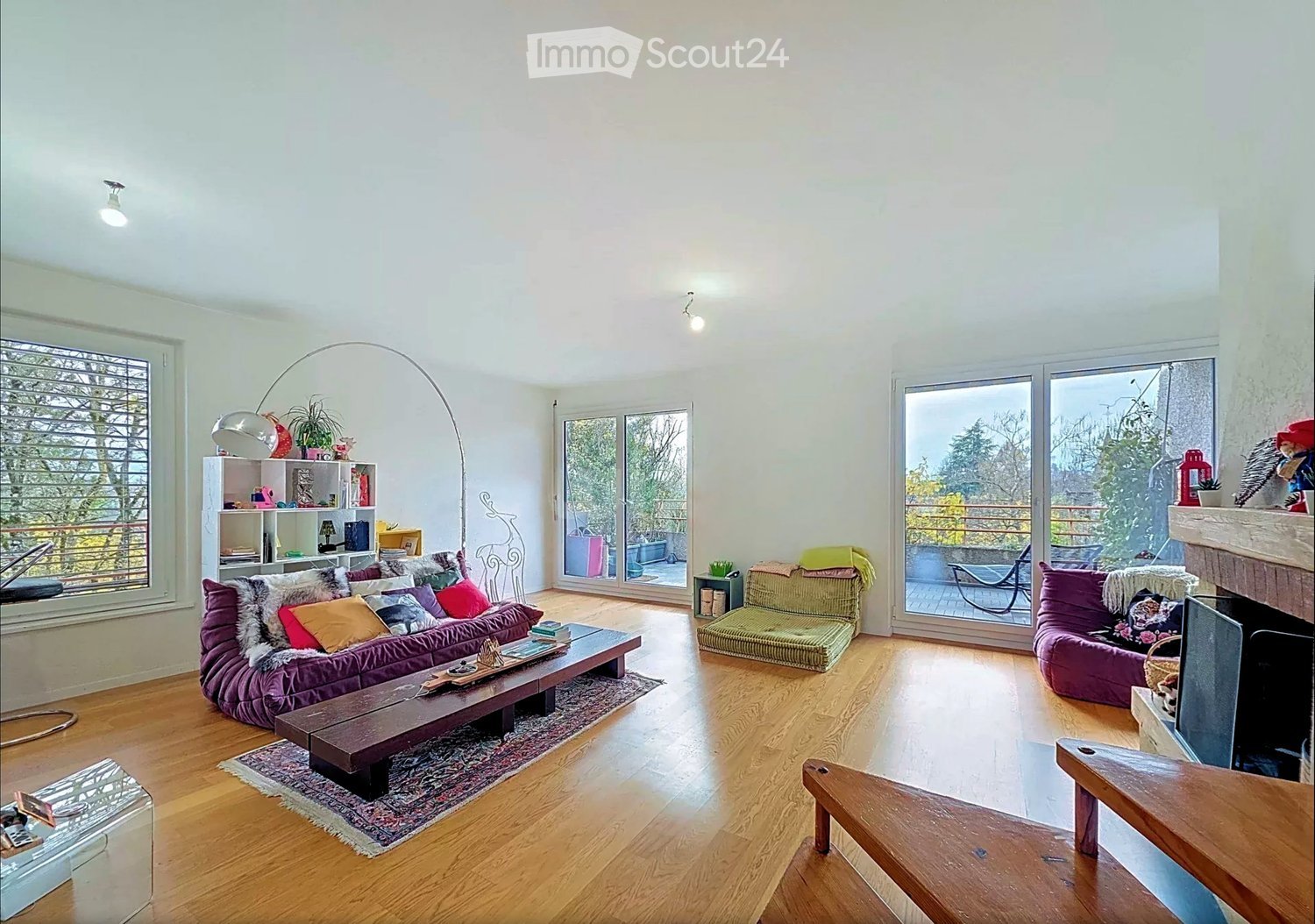 modern style living room, hardwood floors, large windows, sliding doors to balcony, fireplace, glass coffee table, sofa, chairs, rug