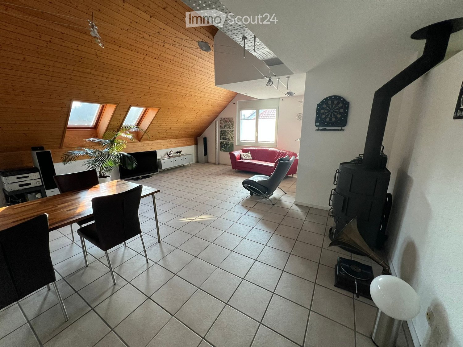 Spacious open-plan living area with wood-paneled walls, tile flooring, large windows, a fireplace, a sofa, and a dining table with chairs.