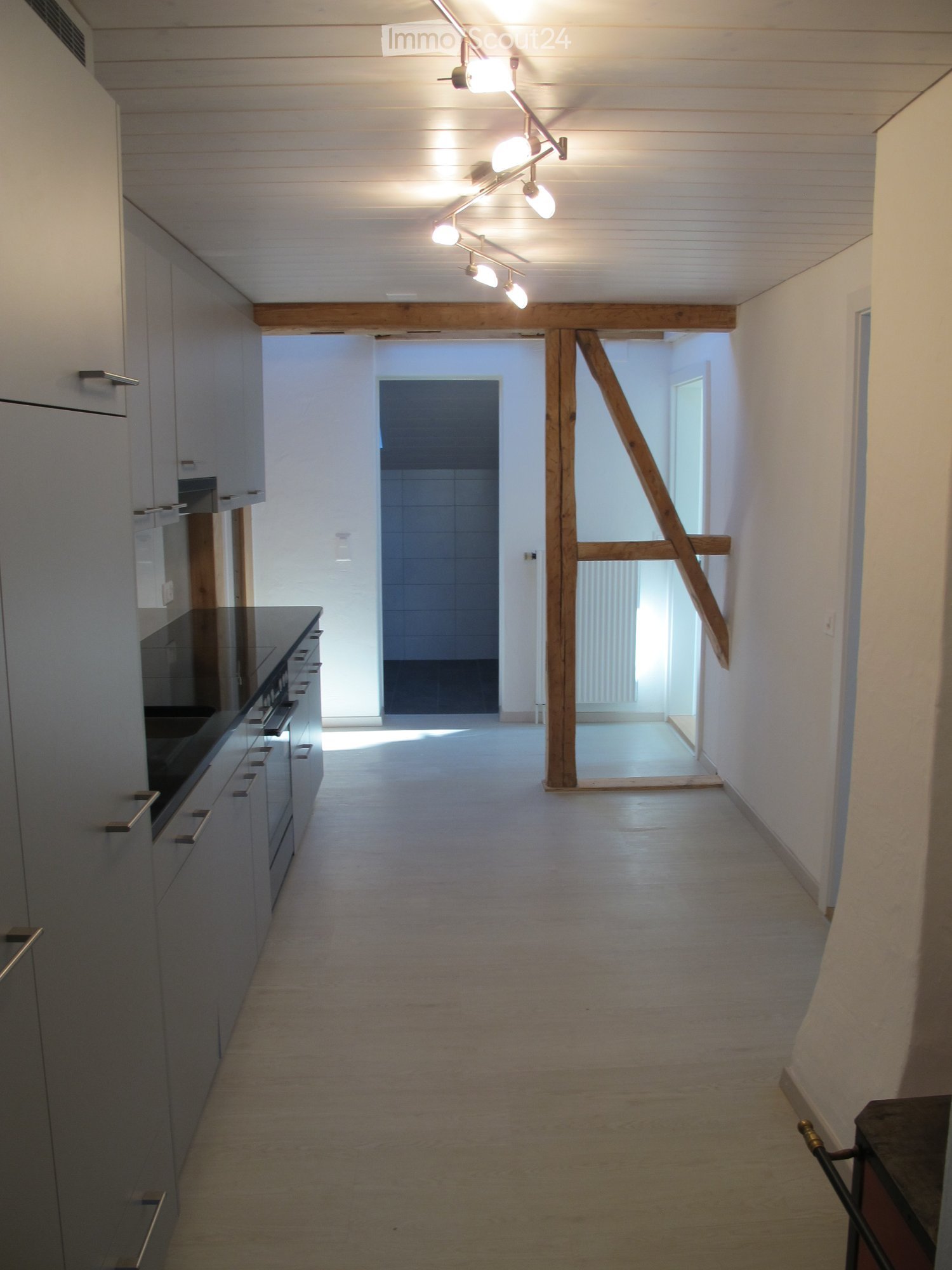 Empty kitchen with white tiled floor, wooden beam, white cabinets, black countertops, sink, appliances
