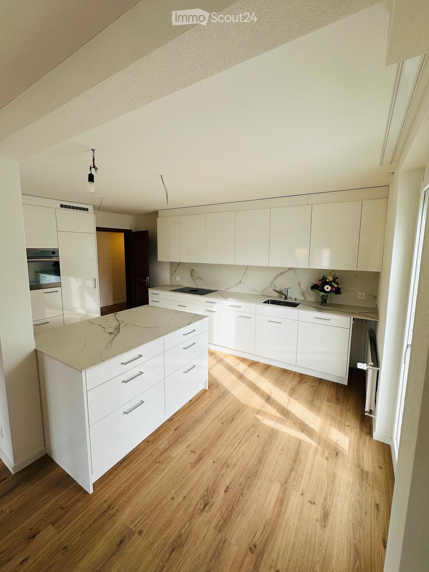 modern kitchen with wooden floor, white cabinets, marble countertop, oven, dishwasher, central island, marble backsplash, flower vase on counter, light fixtures, open doorway