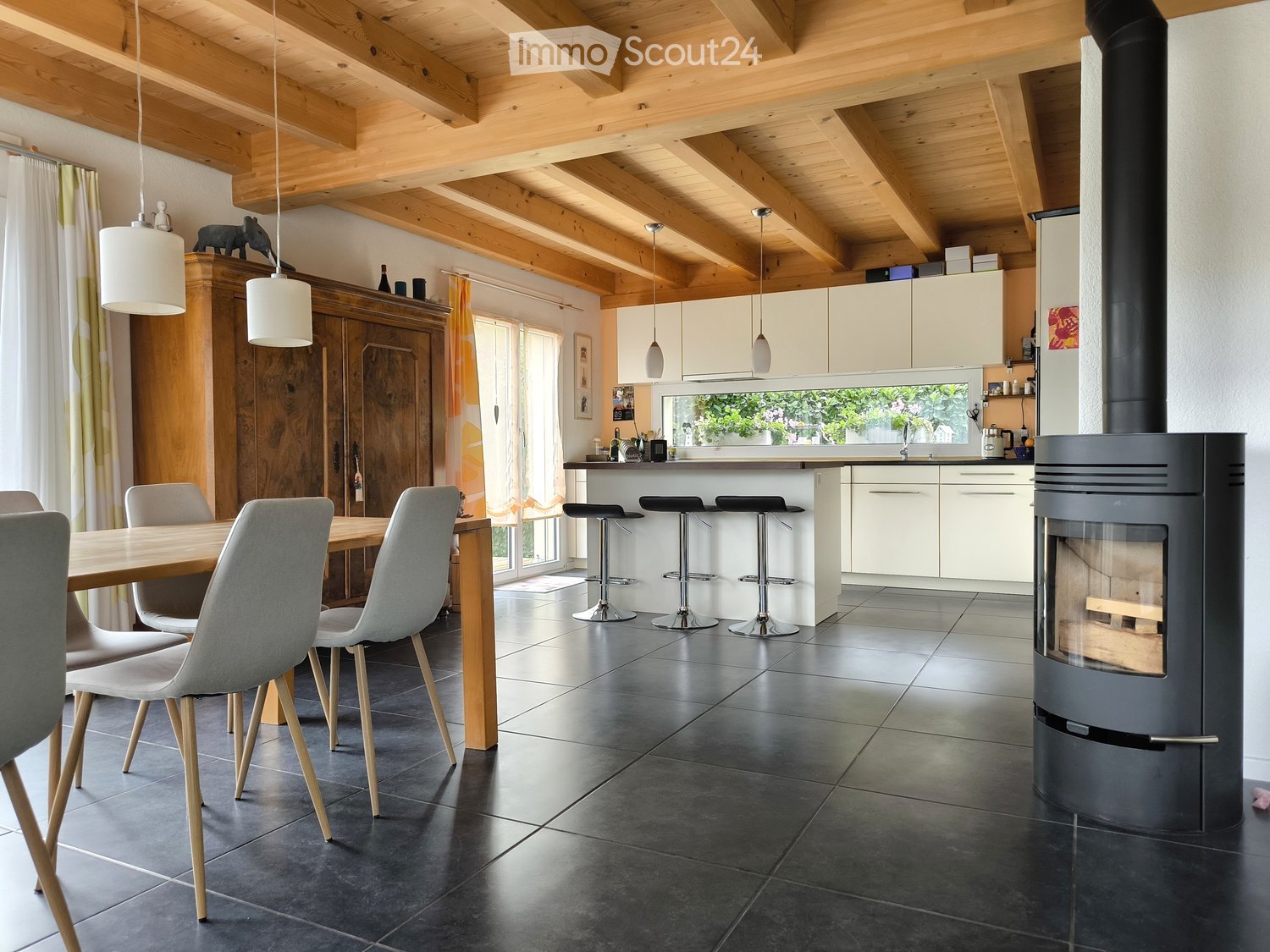 modern open floor plan, dining table with chairs, kitchen counter with stools, wooden beam ceiling, fireplace