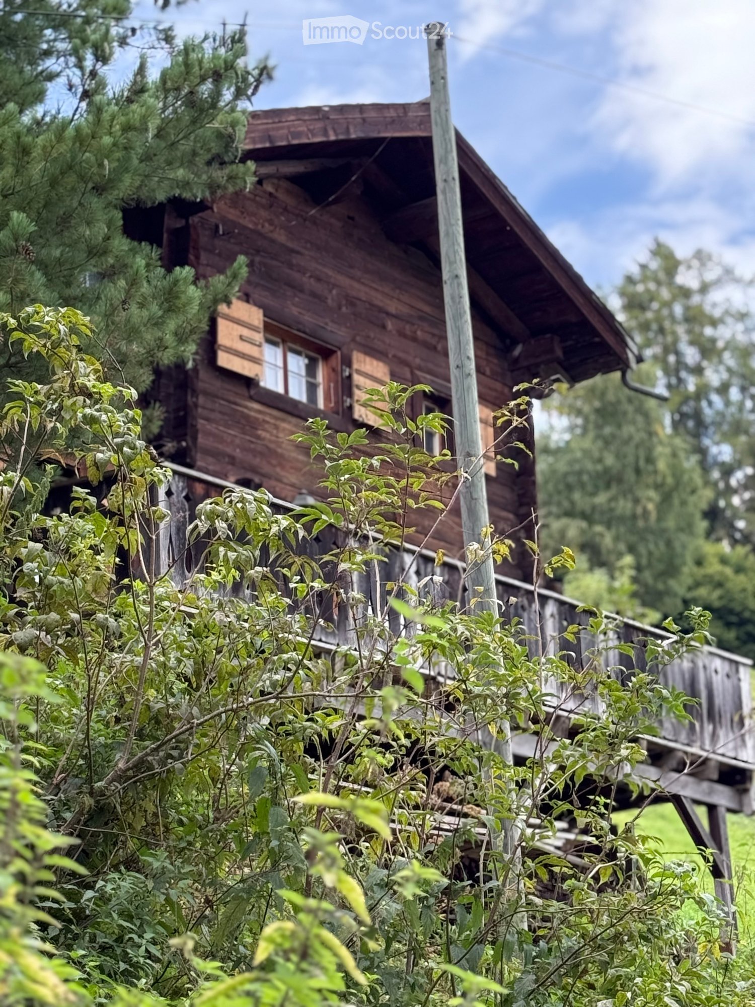 wooden house with gable roof, balcony, surrounded by greenery