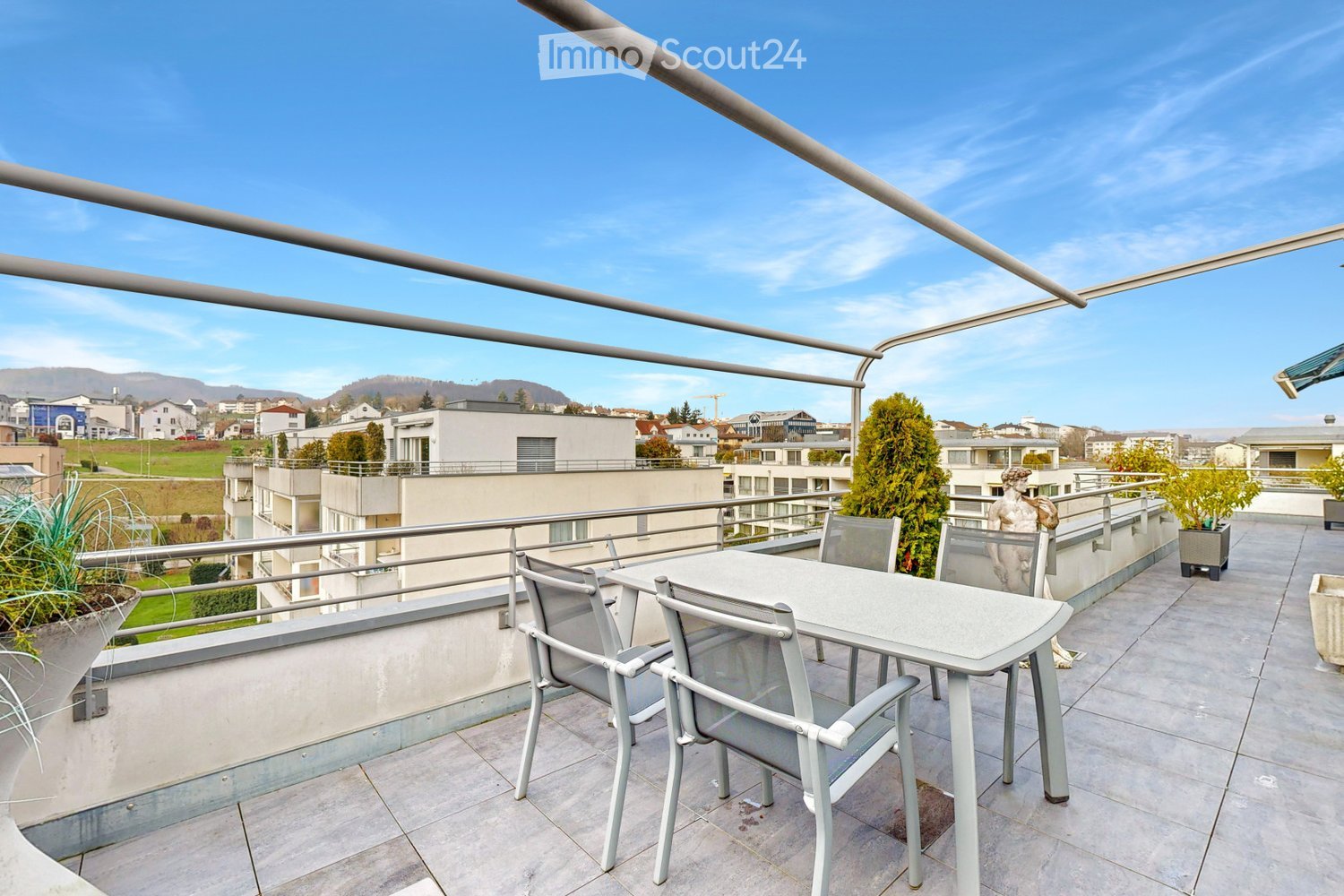 Table and chairs, potted plants, fencing, tiled flooring, distant view of the city