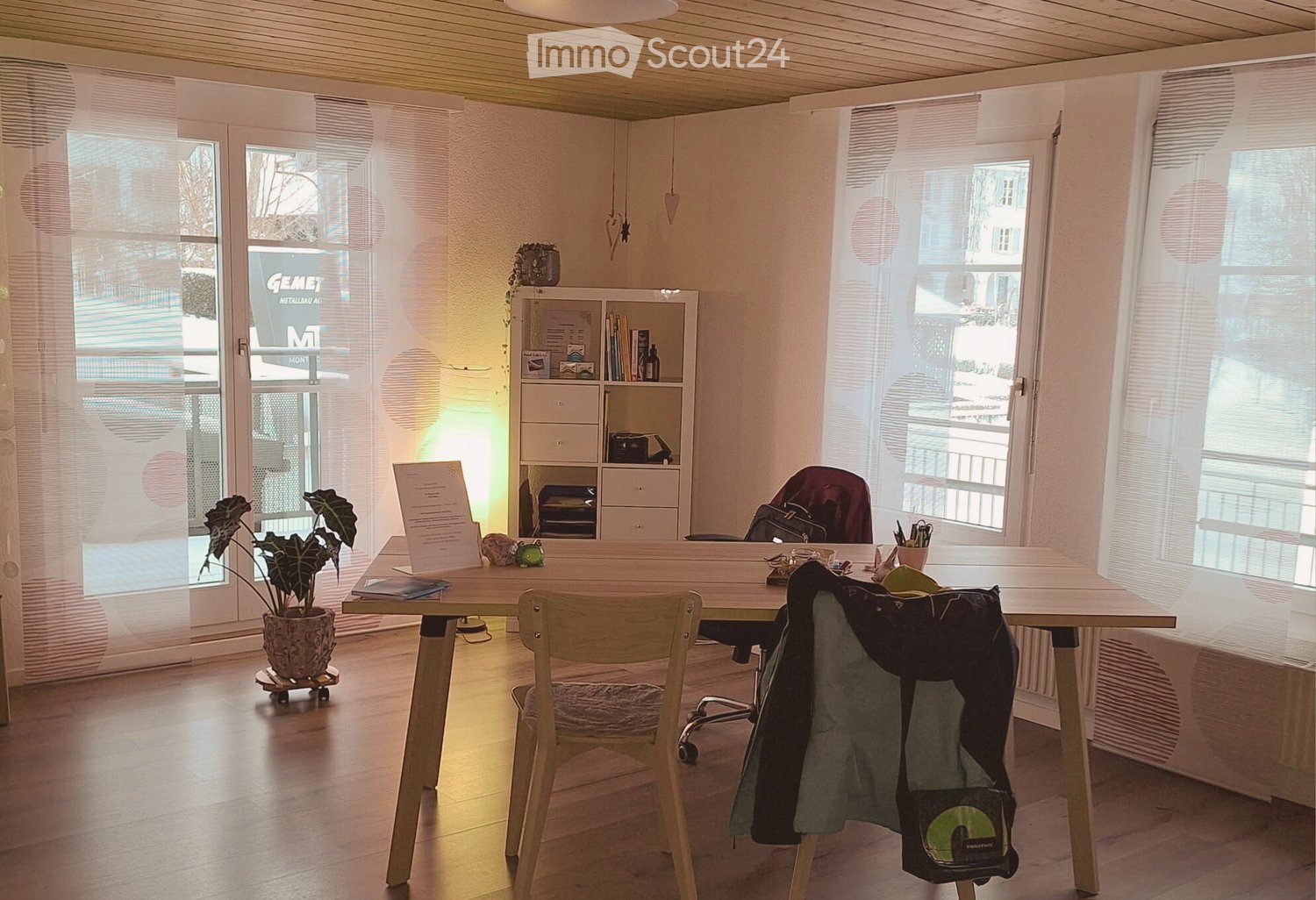 wooden desk with chair, small potted plant, bookcase, glass door leading to balcony