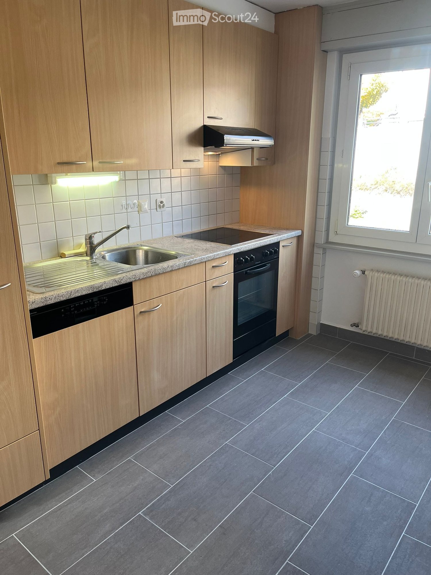 wooden cabinets, granite countertop, black stove, stainless steel sink, dishwasher, light tiles