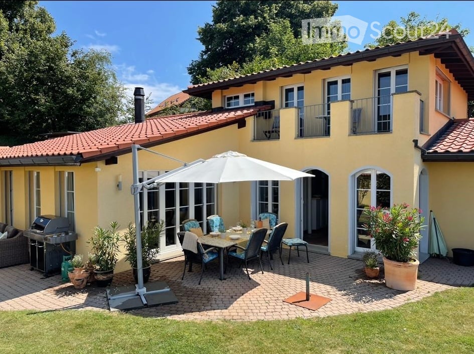 yellow painted house, red tiled roof, balcony, paved outdoor dining area, dining table, chairs, plants, BBQ
