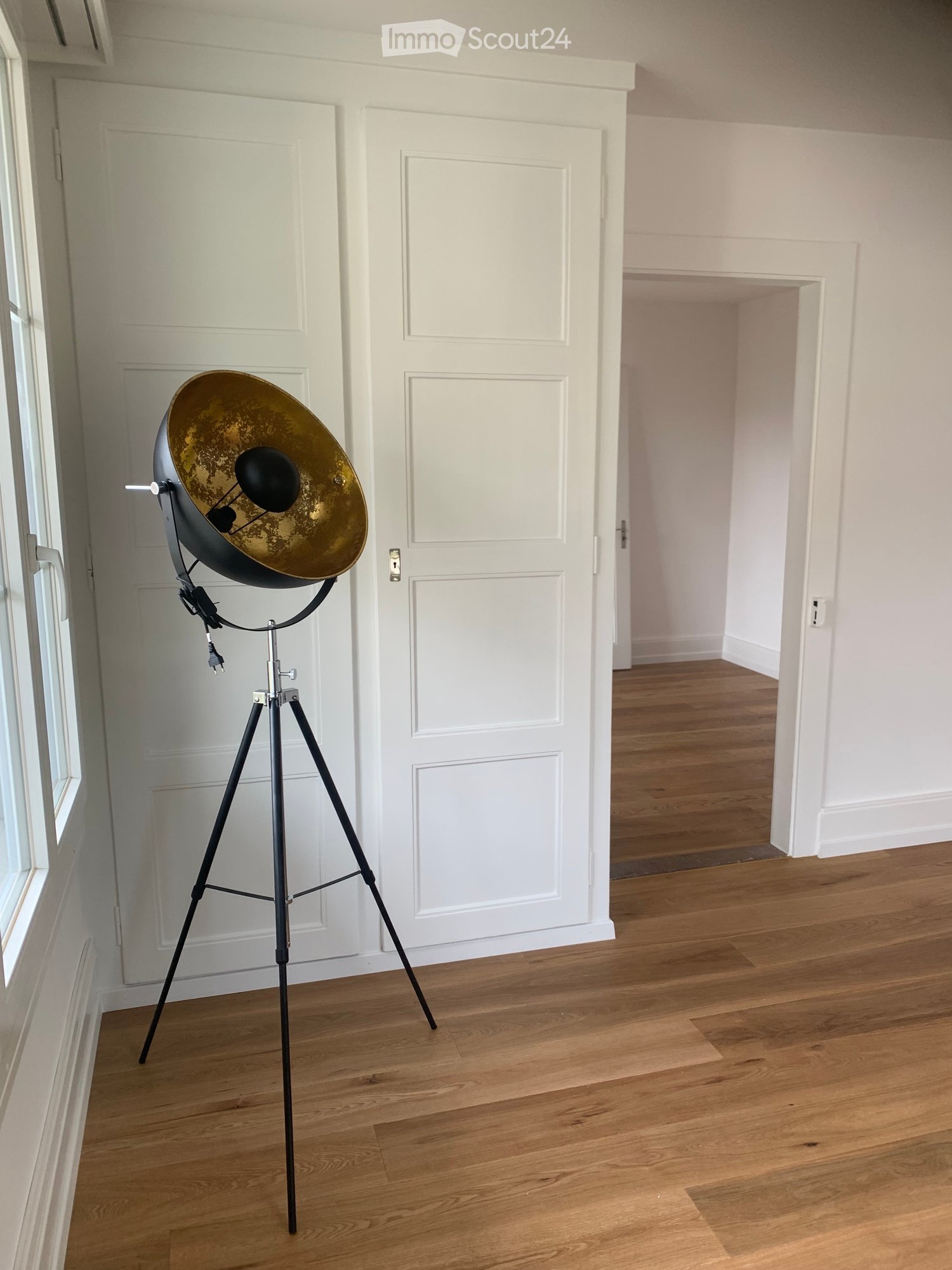 Minimalistic room, wooden floor, a tripod floor lamp, a window, two white doors