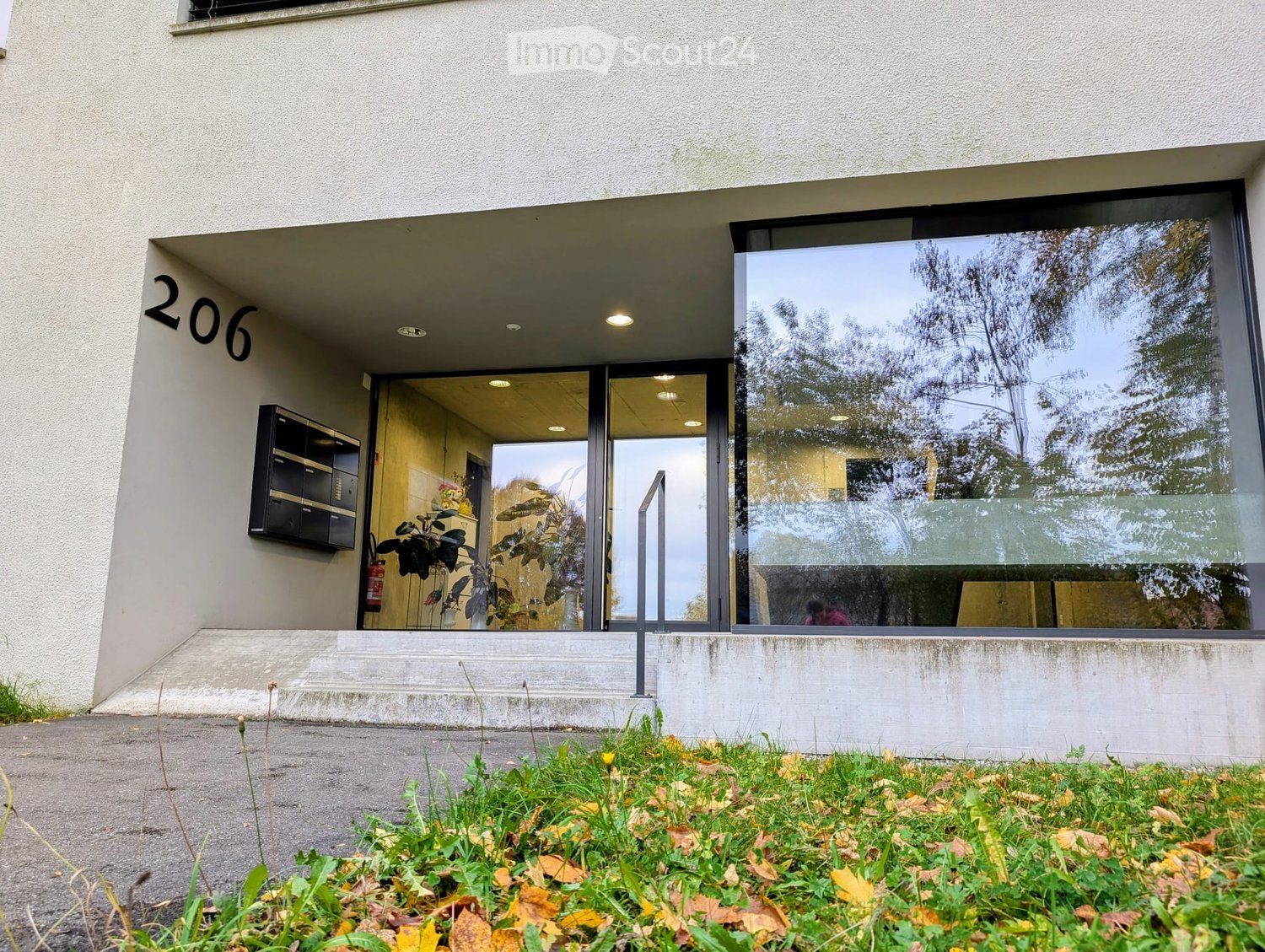 Modern entrance with raised ground floor, large glass windows, and a fire extinguisher.