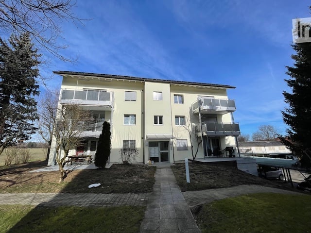 2 story building, light yellow exterior, solar panels on roof, balconies, cars parked