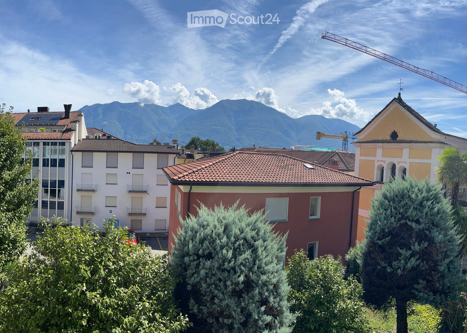 Aerial view of buildings, surrounded by greenery, mountains in the background, solar panels on roof