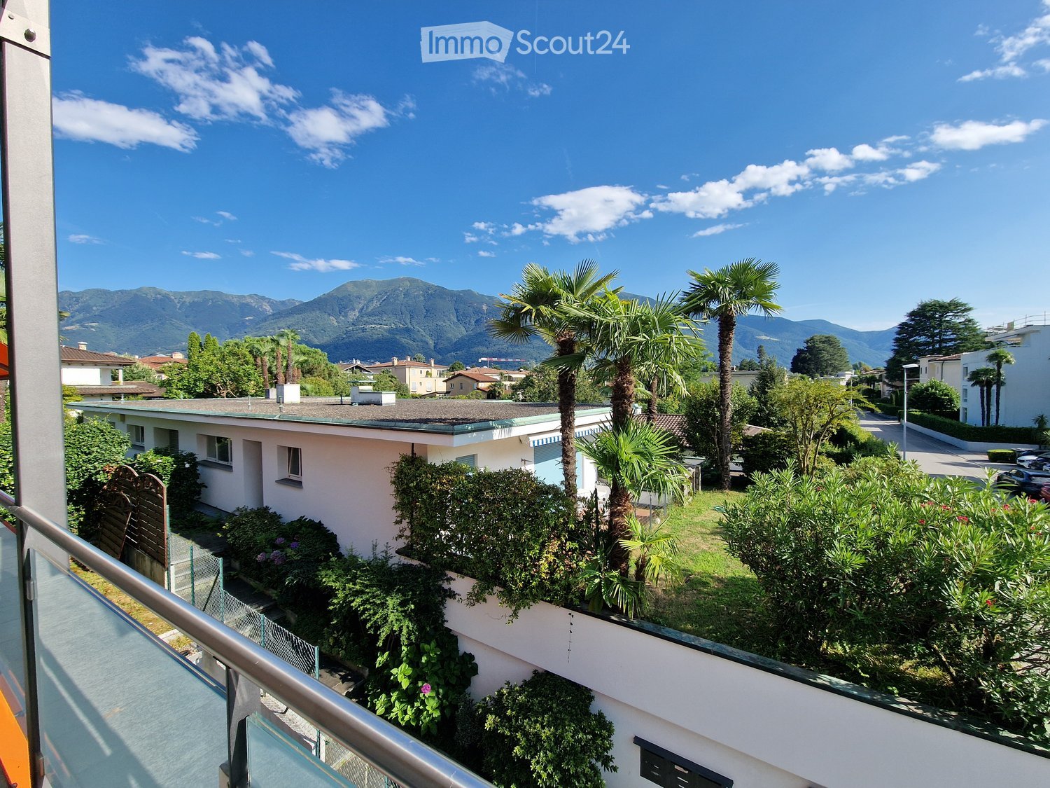 Building with a balcony and terrace, surrounded by lush greenery and mountains in the background.