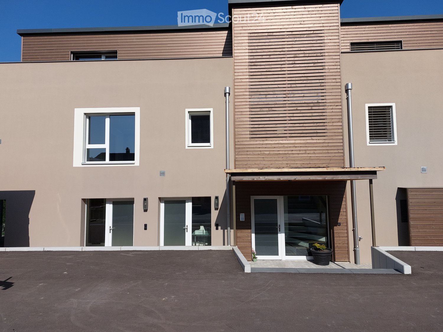 Modern 2-story building, light beige wall, glass windows, glass doors, brown wooden door, two chimneys, parking lot