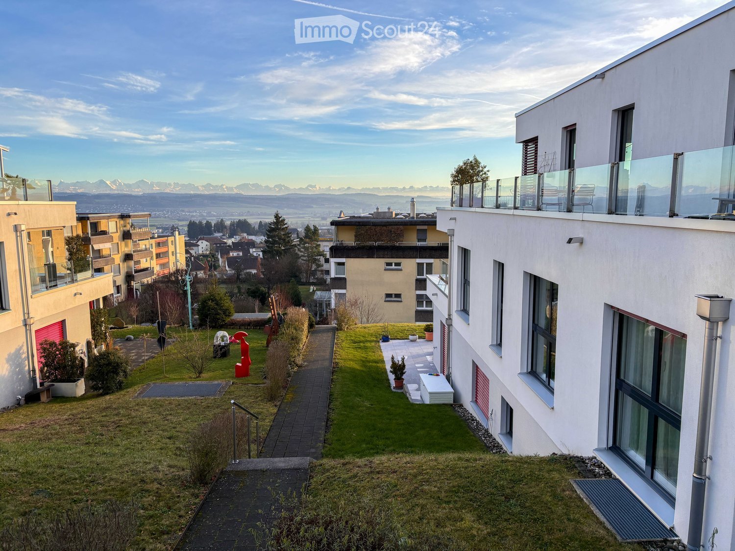 Apartment complex with multiple buildings, terraced design, large garden area, clear view of the mountains