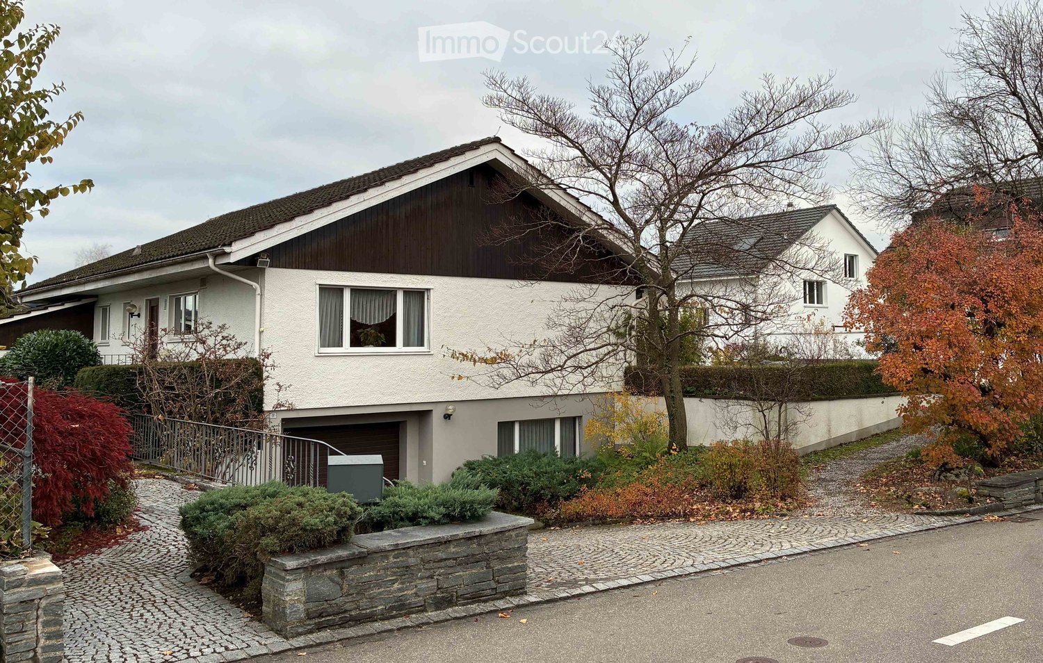 Detached house, white exterior, brown roof, garage, fenced garden, multiple windows, pathway to entrance, small shrubbery, neighboring houses visible