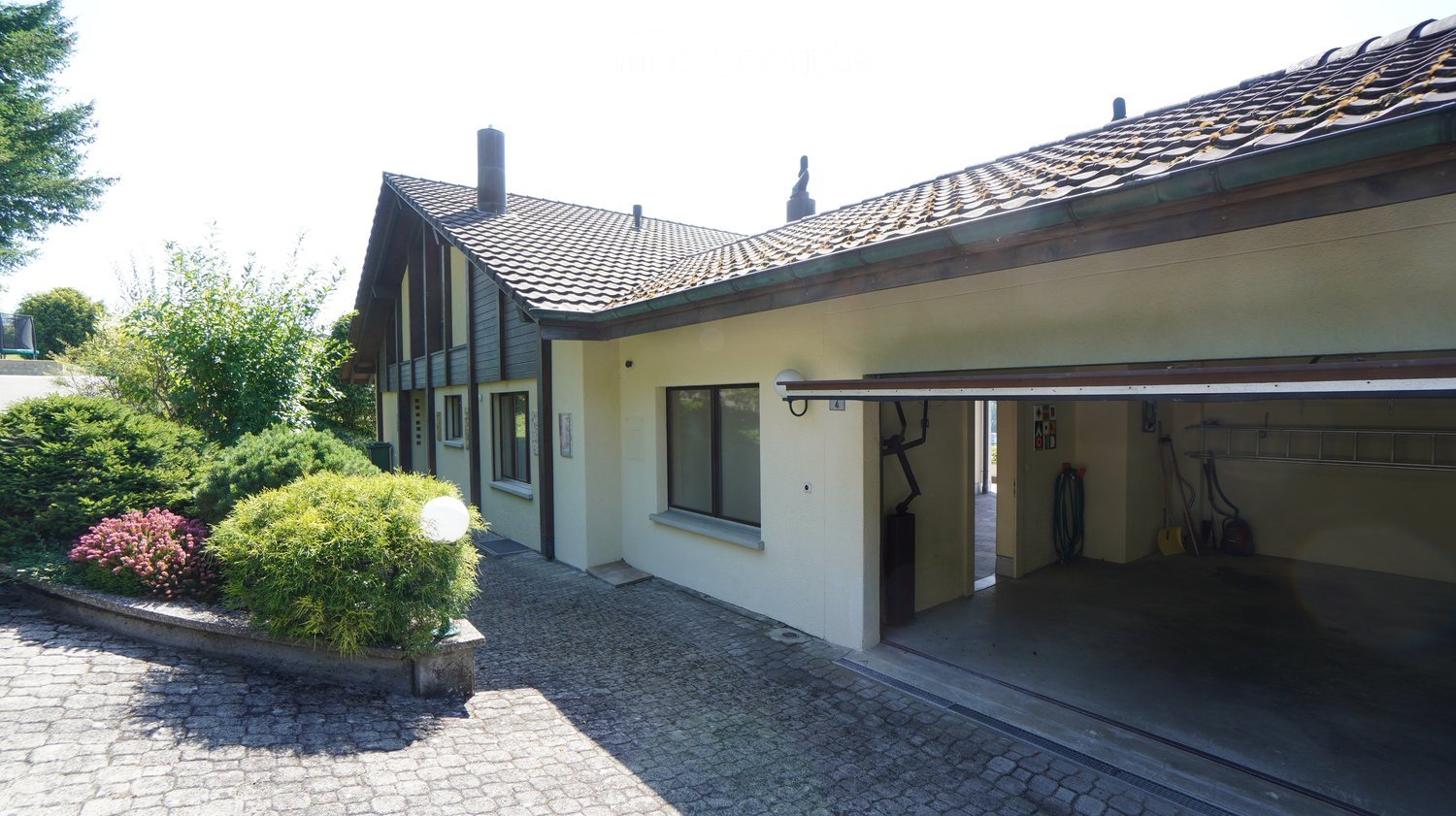 2 story house, beige, open garage, plants, gravel driveway