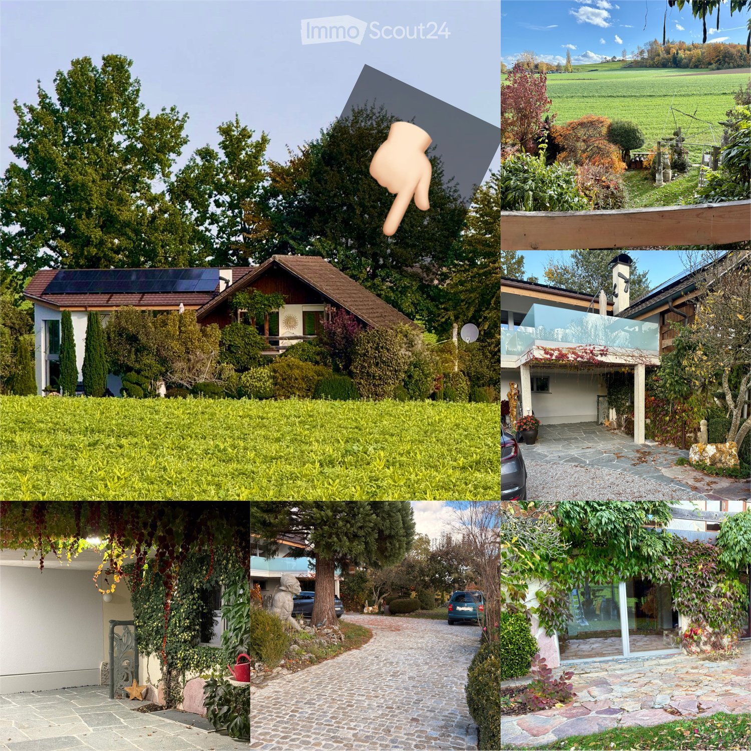 A property features a raised ground floor and an outdoor balcony/terrace. It is surrounded by lush greenery and offers a panoramic view of the field. A large driveway with several cars and a wide open field in the background.