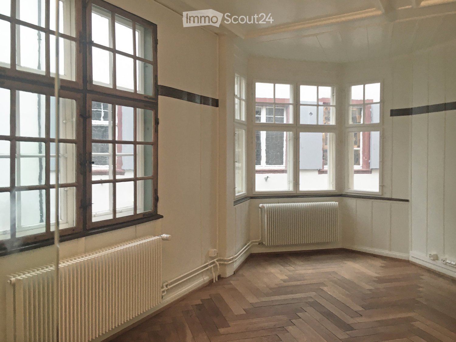 empty room, wooden herringbone floor, large windows, white walls, white radiators