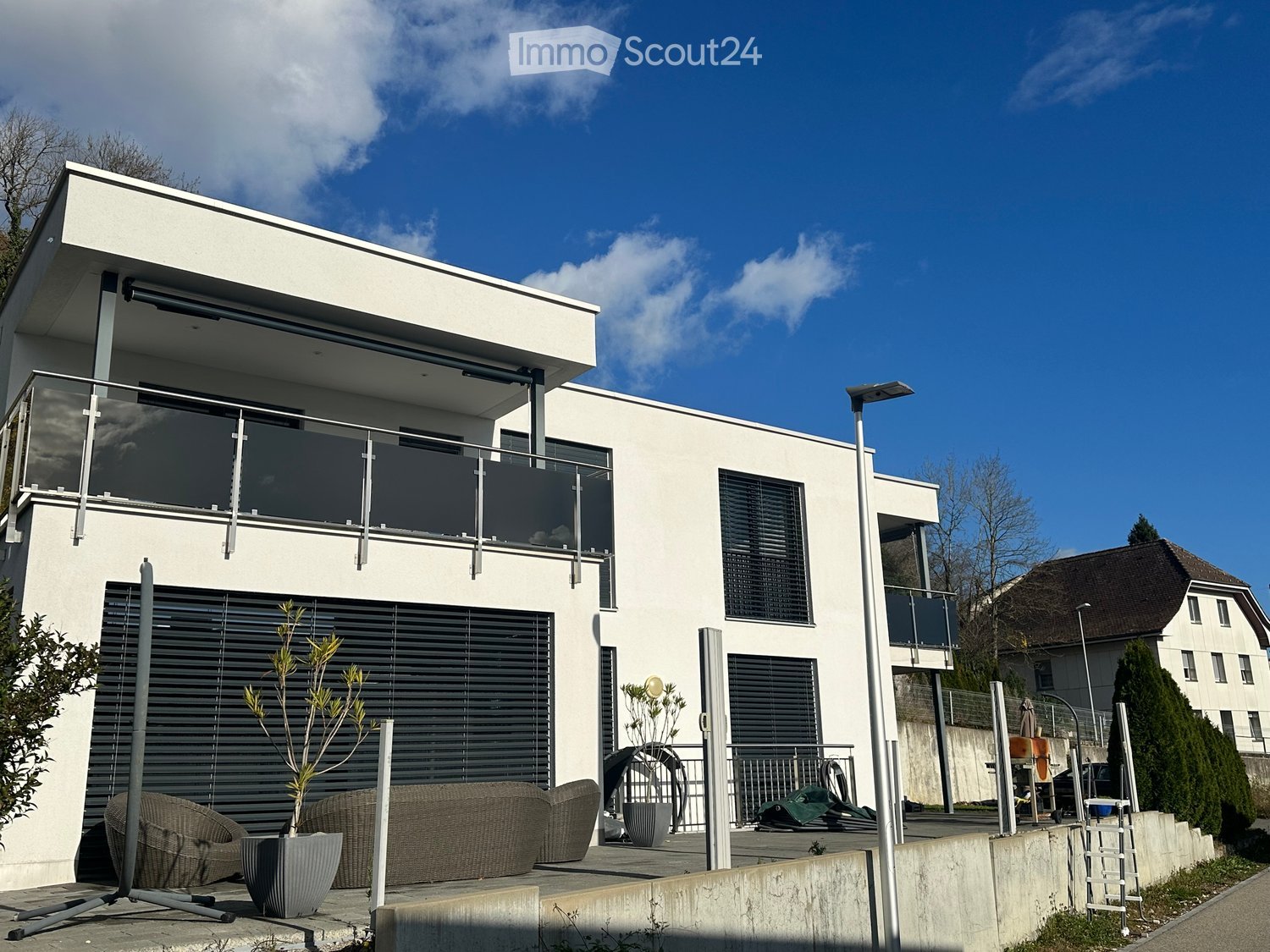 Modern white two-story house with balcony and garage, surrounded by plants and lawn