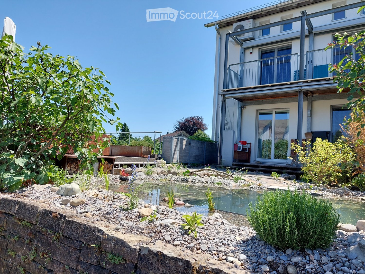 Small artificial pond, shrubs, stone wall, building with balcony