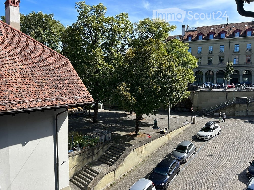 Building with a view overlooking a tree, stairs, parked cars and a building.