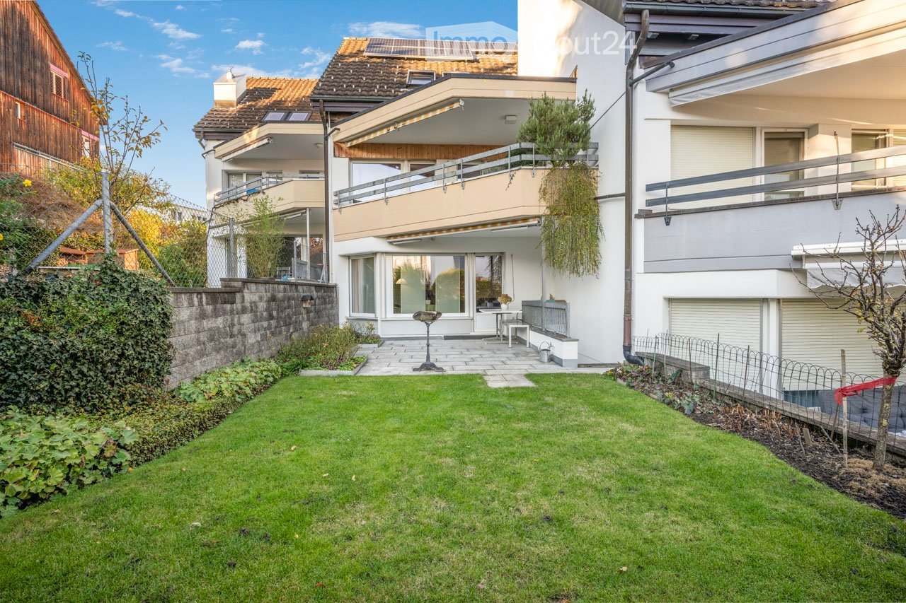 2 story white building with brown roofs and solar panels, balconies, green grass, small garden