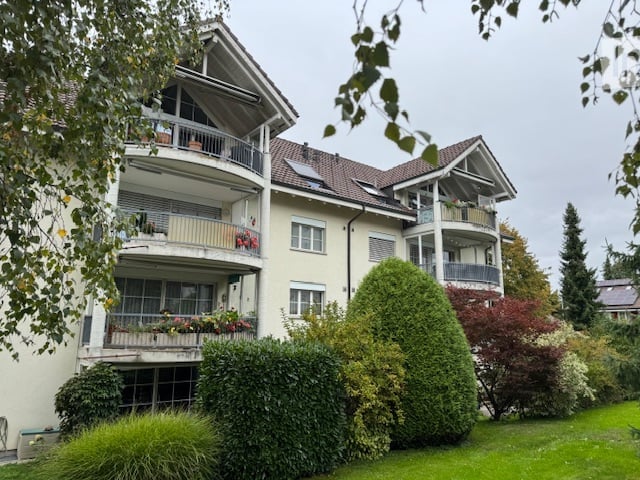 3 story apartment building, white exterior, multiple balconies, large garden, solar panels on the roof