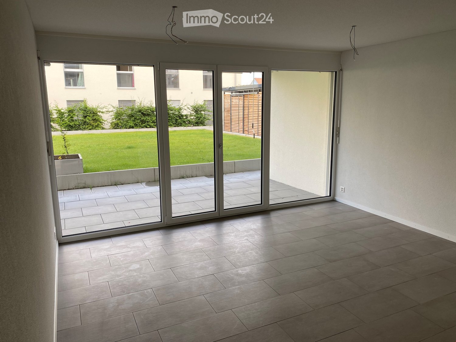 empty room, sliding glass doors leading to balcony, tile flooring, outside area with grass and plants