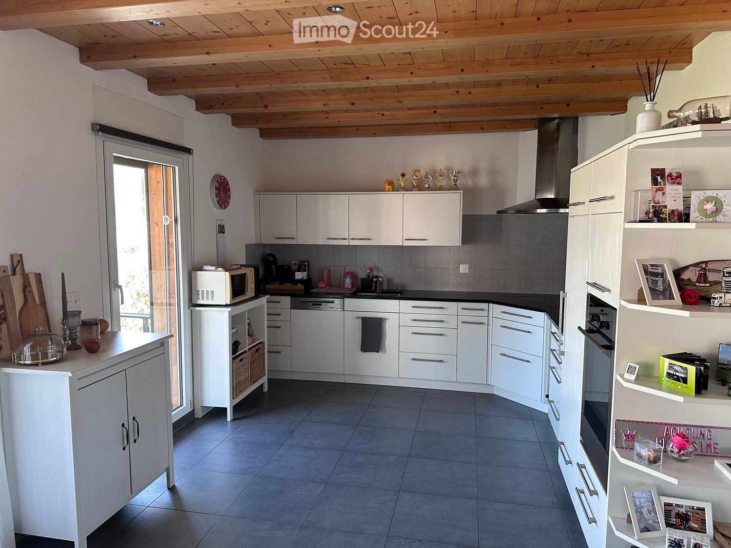 White kitchen with modern appliances, wooden ceiling, sliding glass door, black countertops, white cabinets, kitchen island, stainless steel sink, modern fixtures