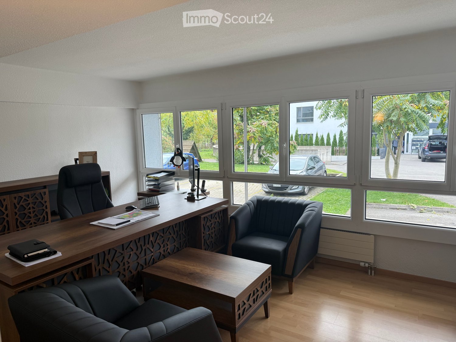large windows, black desk, three black chairs, one wooden coffee table, wall mounted radiator, parquet floor