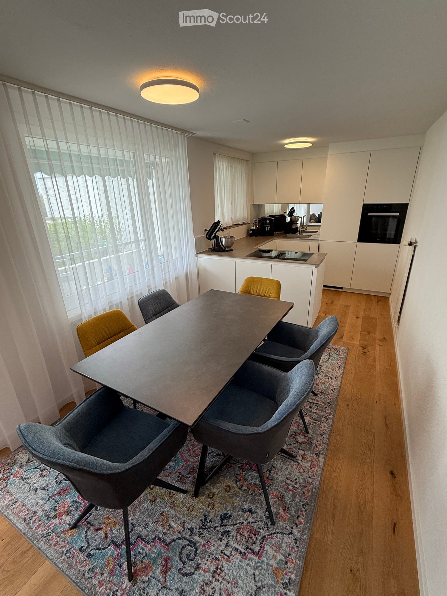 Rectangular table, 6 chairs, white cabinets, modern appliances, open plan to kitchen, carpet, windows with curtains