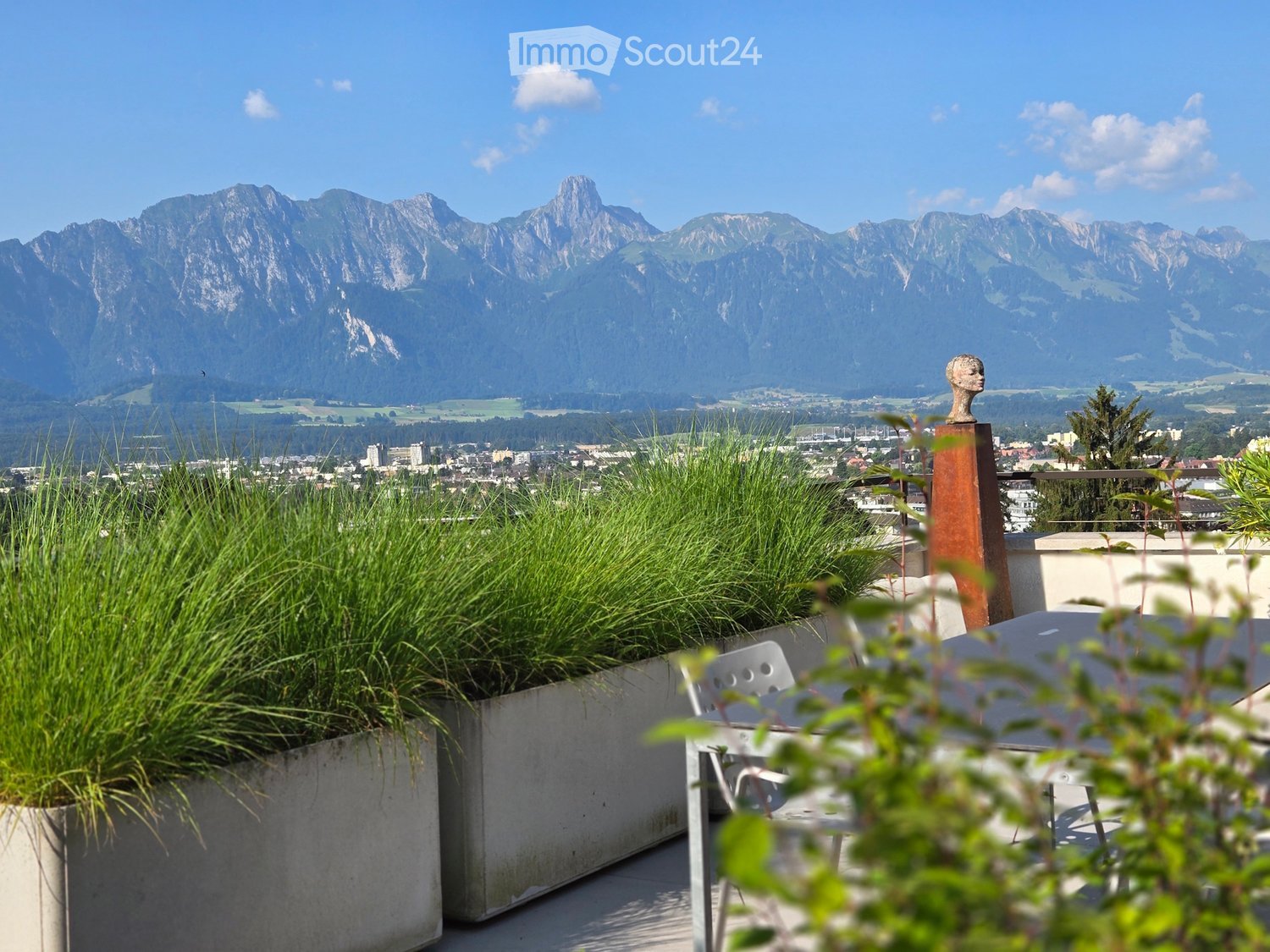 Terrace with concrete planters, table and chairs, view of mountains and city