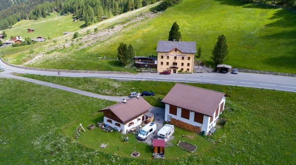 Two houses on hill top, one has larger house on left and smaller house on right, road and vehicles visible, trees, greenery