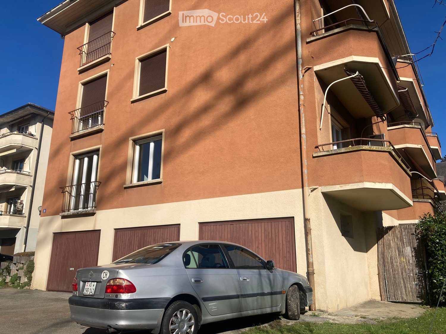 3-story building with balconies, car parked in front of the garage entrance, small front yard
