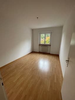 Empty room with hardwood floors, white walls, and a window with a view of trees.