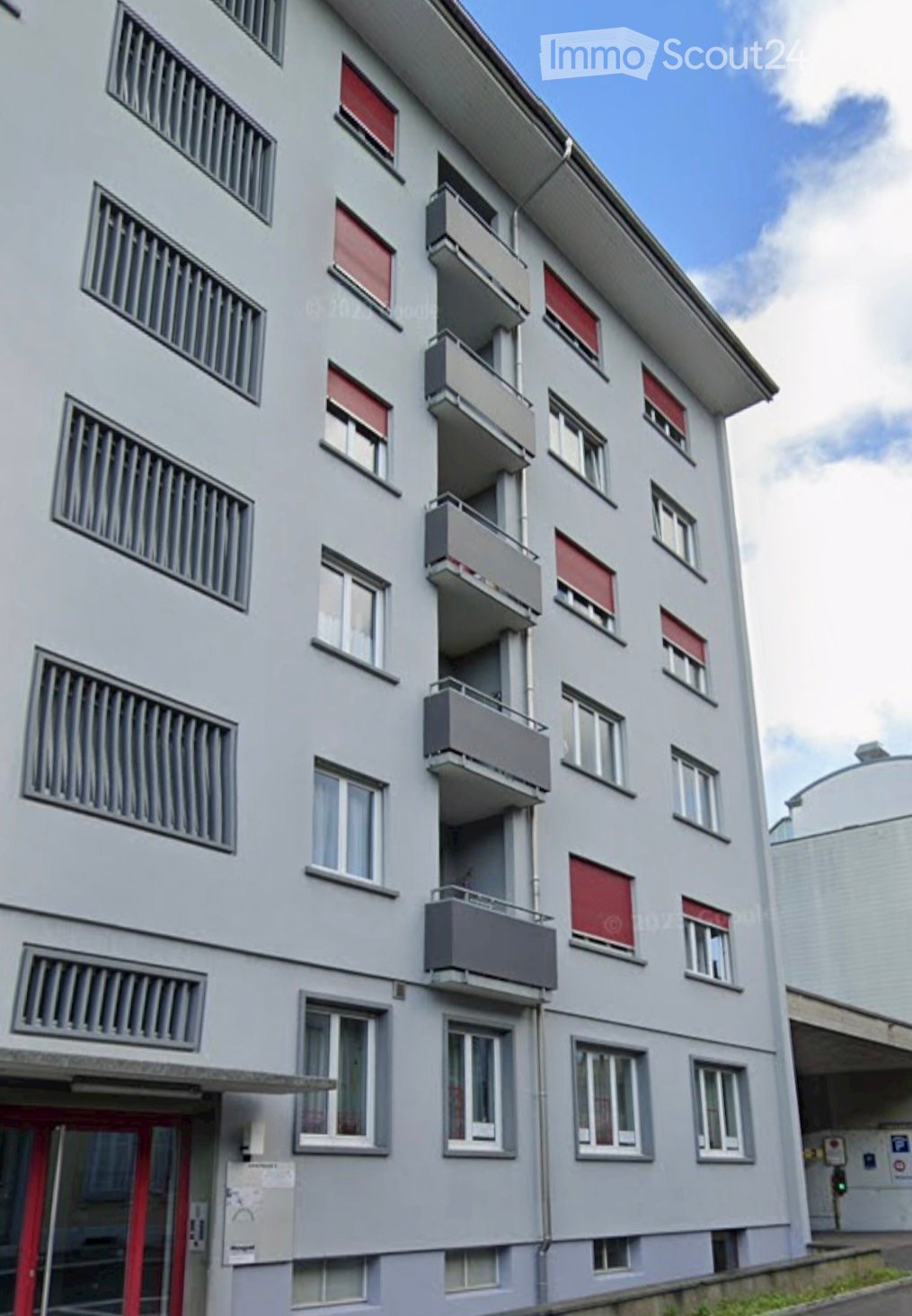 multi-storey building, gray exterior, balconies, red windows, red entrance door