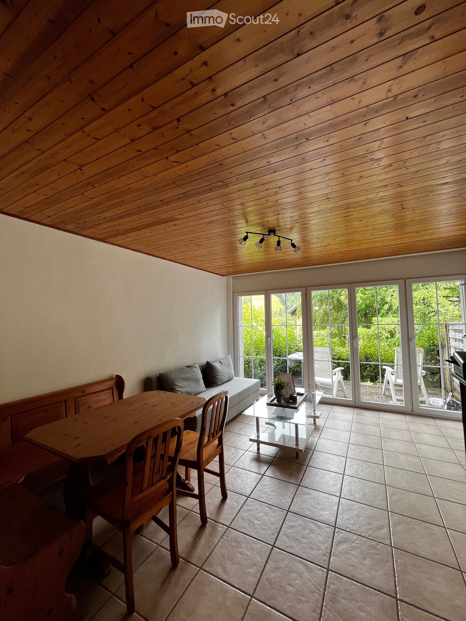 living area with dining table, sofa, large glass doors leading to balcony, tiled floor, lamps, potted plants, wooden ceiling
