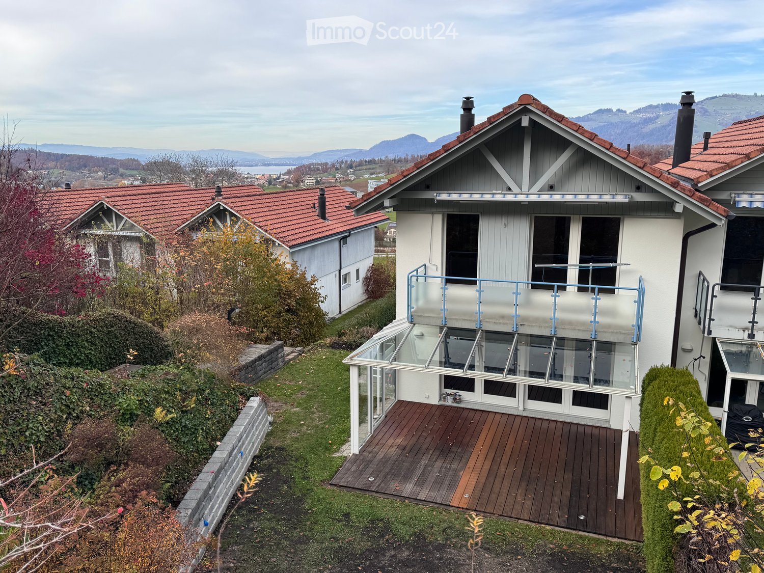 2 story white house, red tile roof, wooden deck, covered glass terrace, mountains in the background