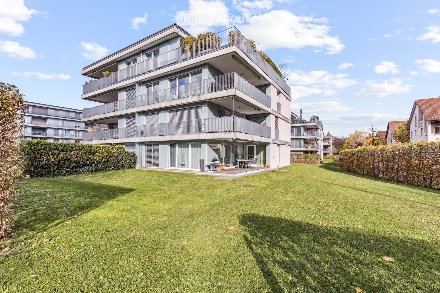 3-storey apartment building, glass windows, balconies, surrounded by hedges, well-maintained lawn