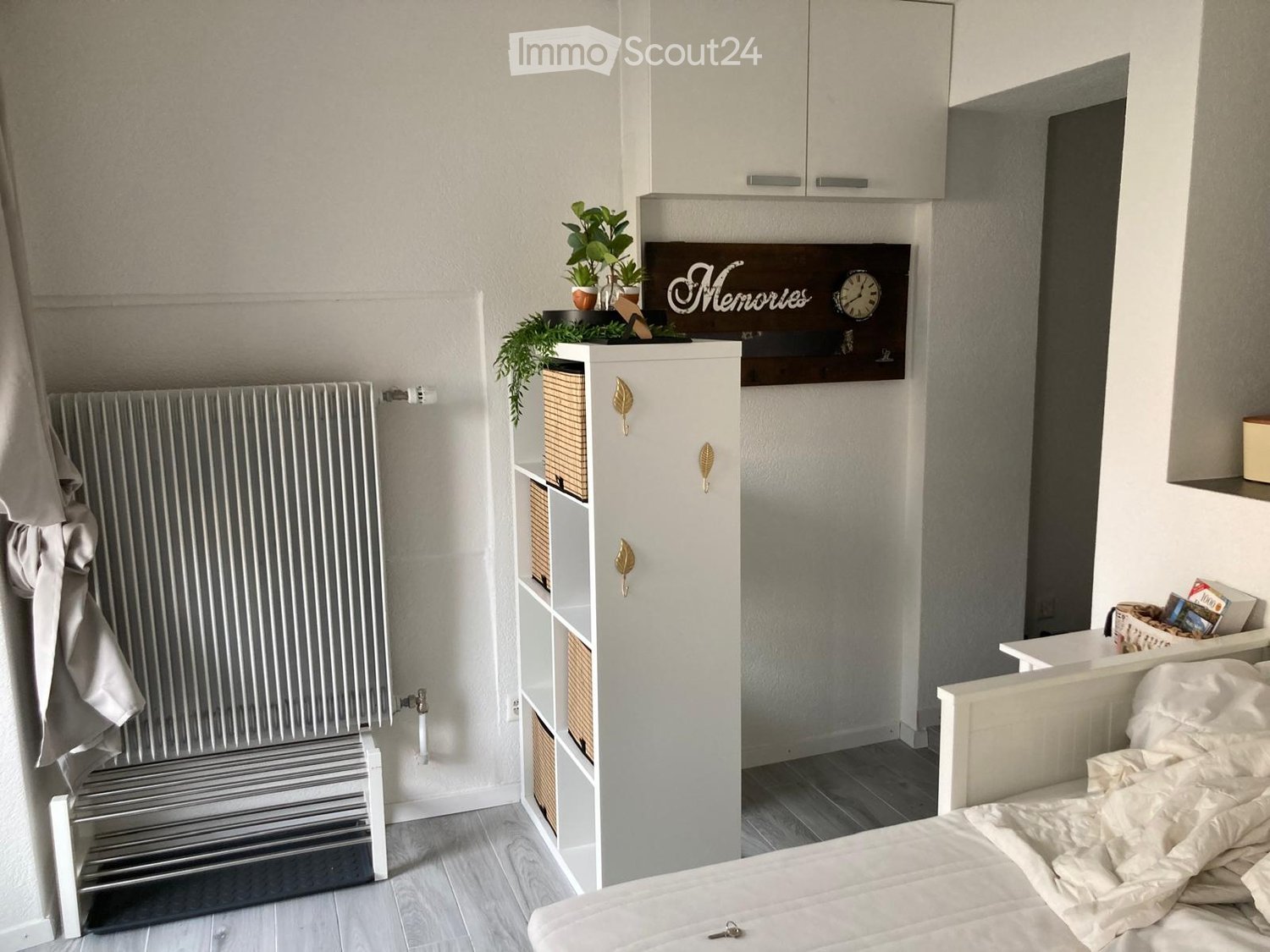 bedroom with white shelves, plant on shelf, white bed, white radiator, towel on radiator