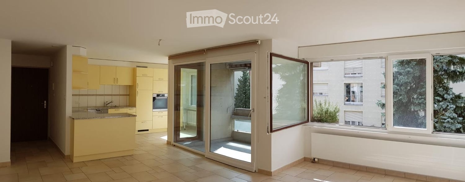 Empty room, sliding glass doors, balcony, kitchen area with appliances, tiled floor, natural light from windows