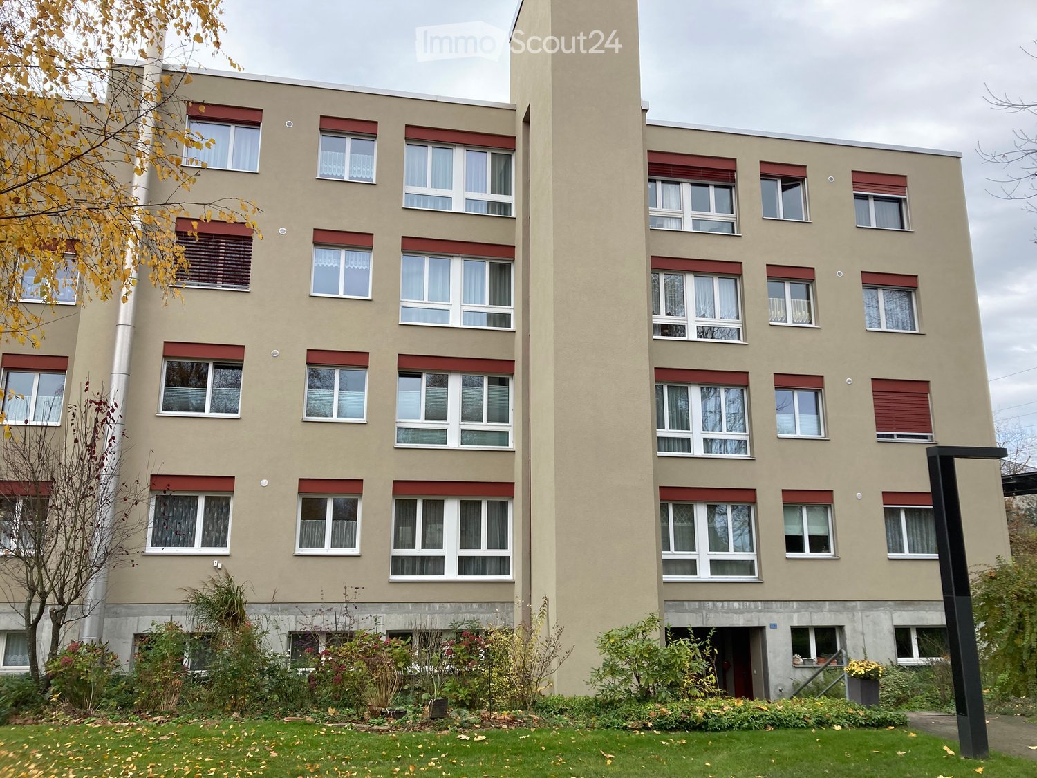 5-story building, brick exterior, windows with white frames, red window trims, entrance with greenery