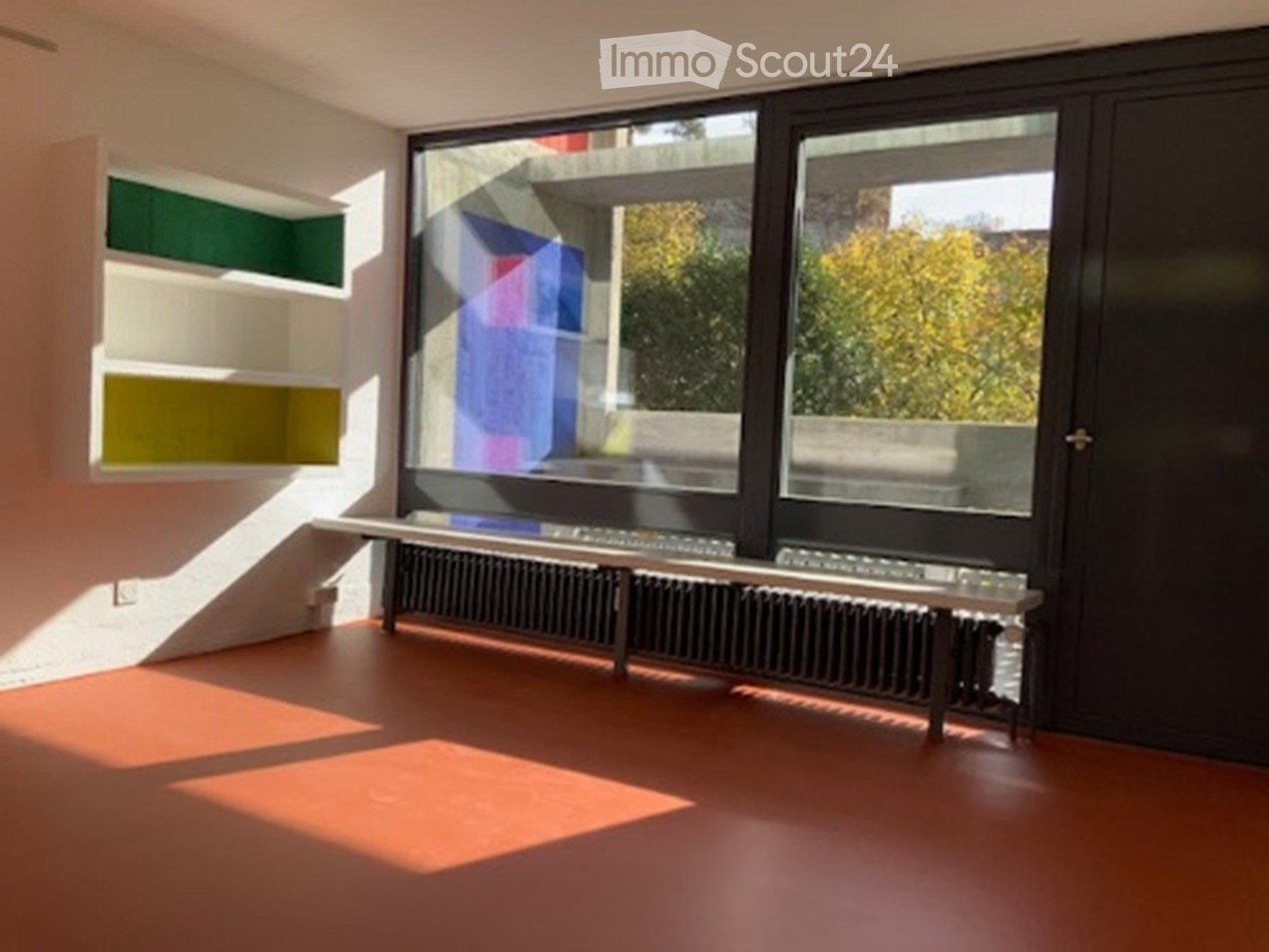 empty room with large windows, orange floor, built-in shelves, radiator