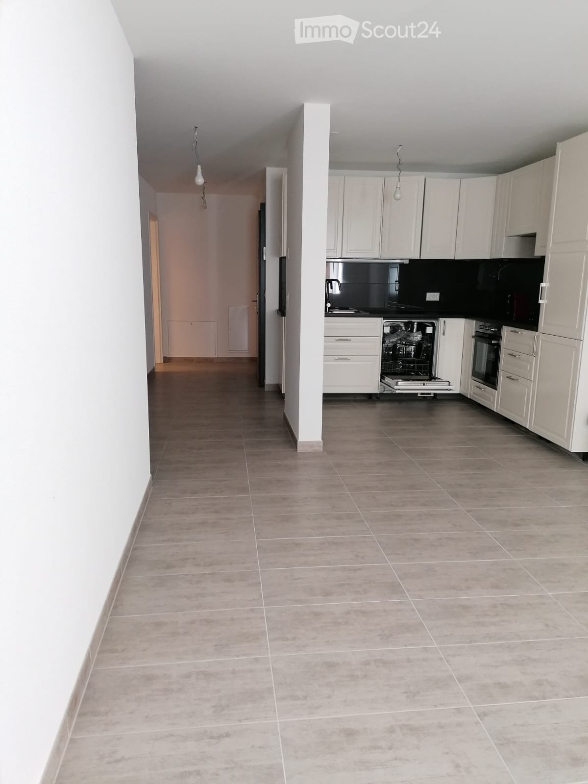 Empty kitchen with gray tile flooring, white cabinetry, and integrated dishwasher and washing machine.
